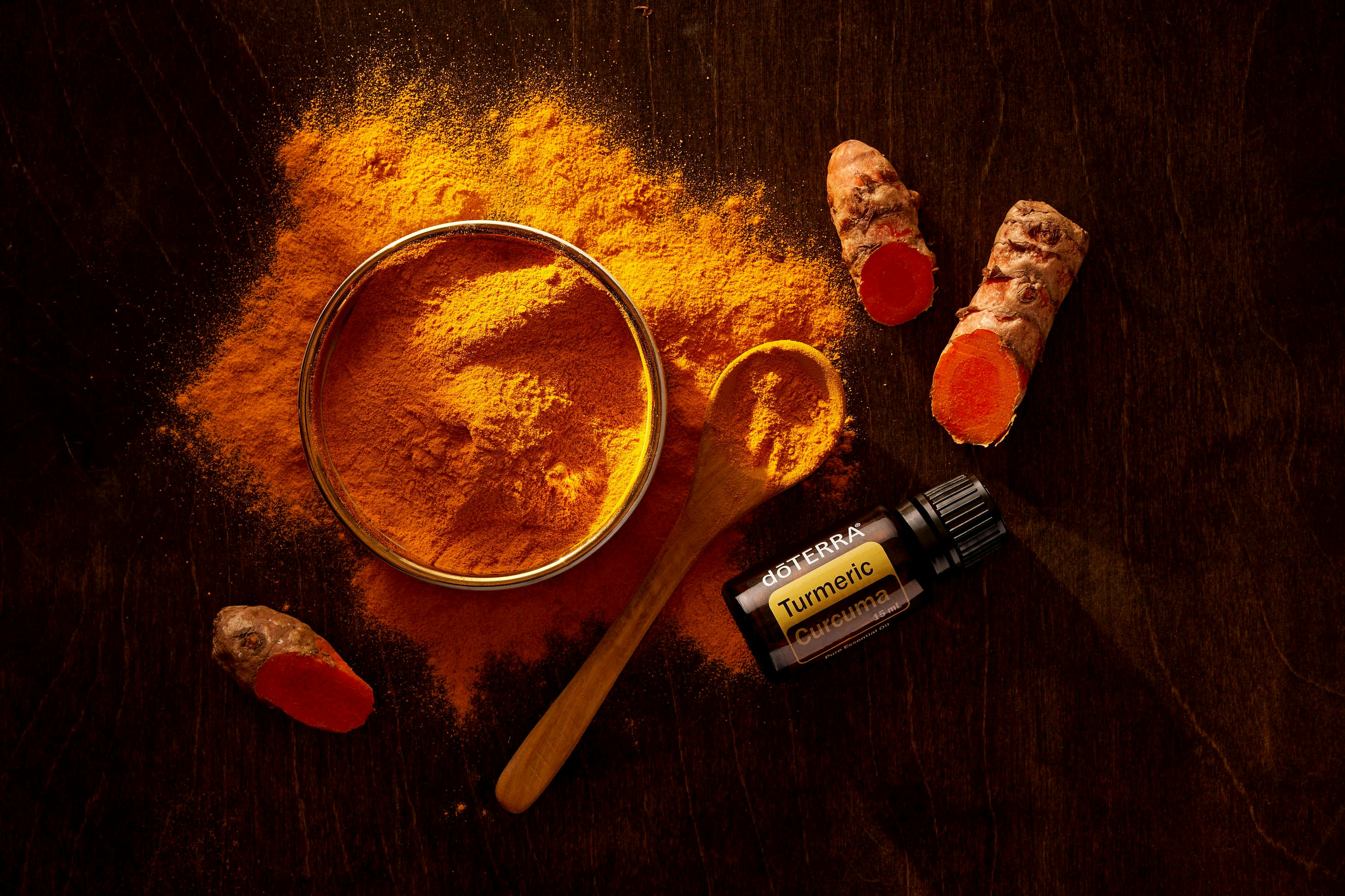Top view of turmeric powder, curcuma roots, and essential oil on wooden surface.