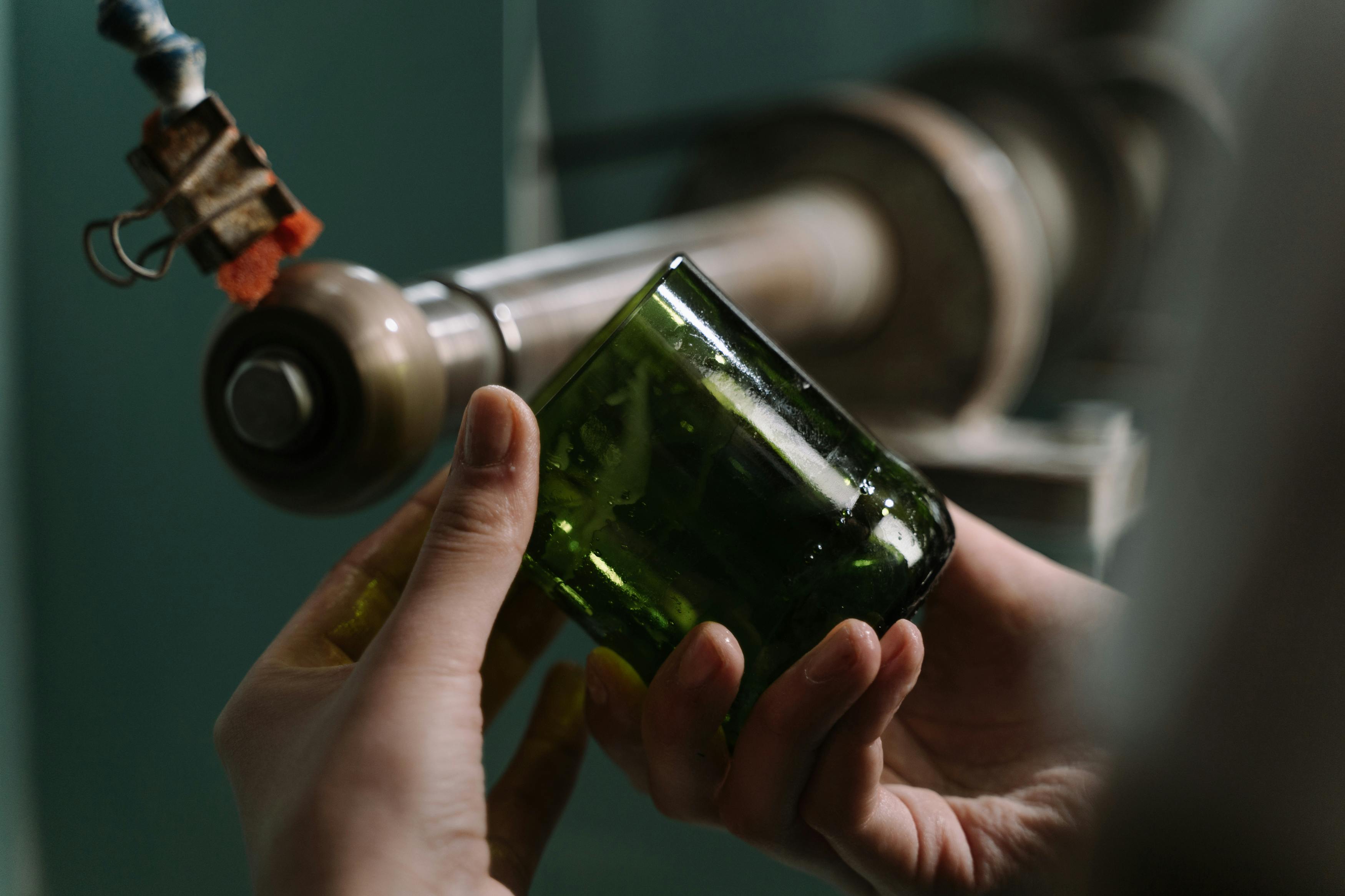 Hands crafting a glass bottle with precision on a cutting machine in a workshop.